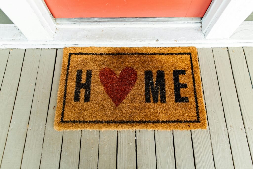 Doormat with 'Home' written and heart symbol on wooden porch.